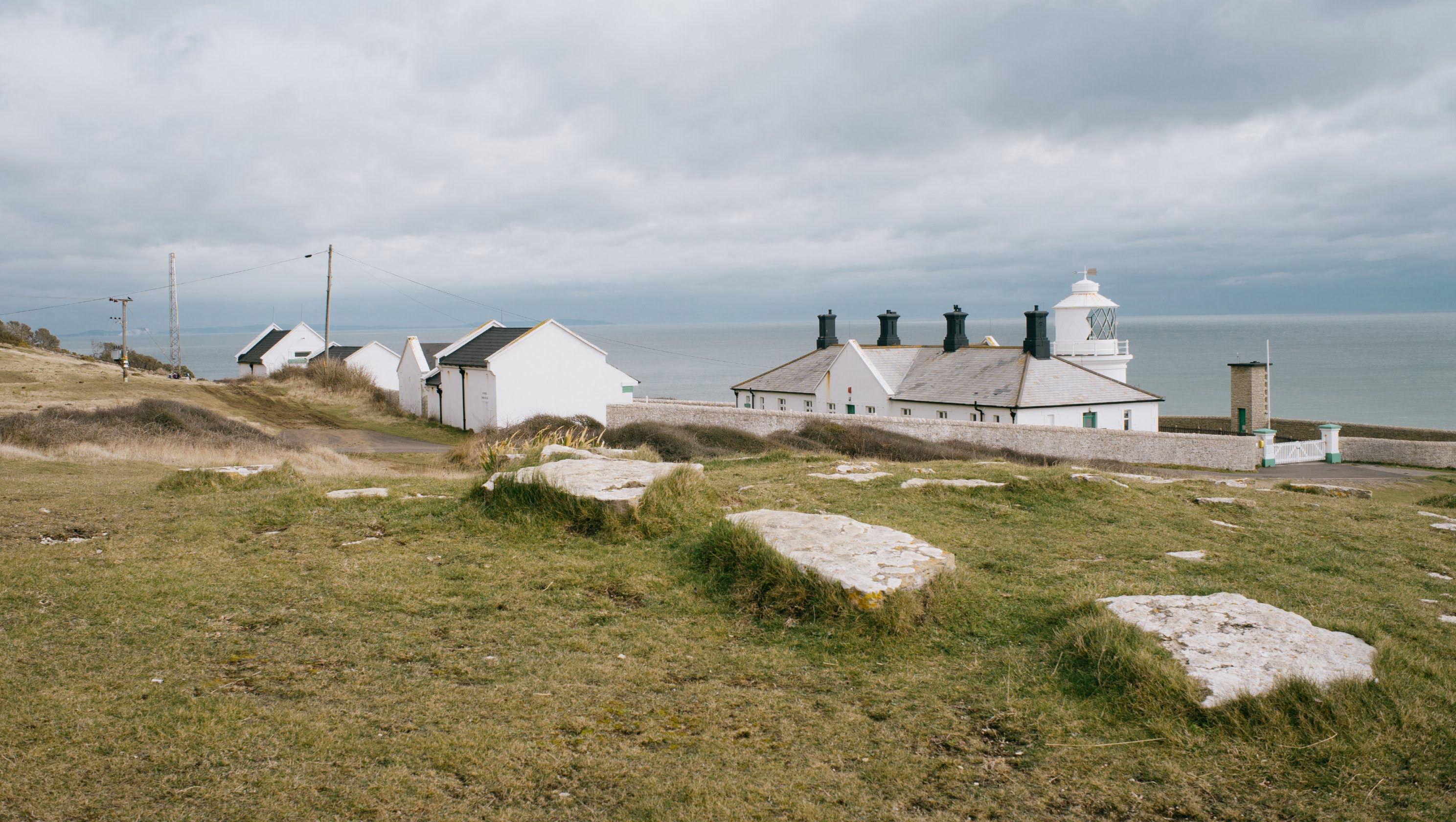 A wide shot of a series of white painted huts with a lighthouse on the right hand side, looking out to see